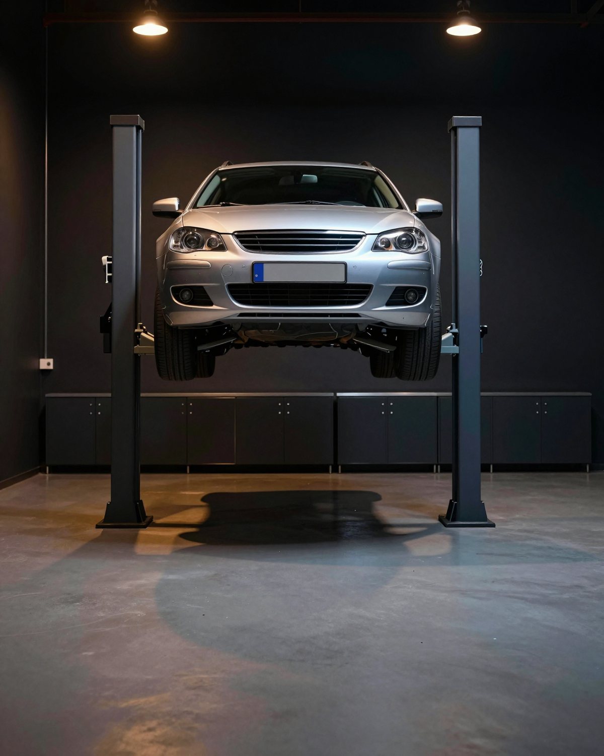 A silver car raised on a two-post lift in a spotless workshop bay, closed tool cabinets along the back wall