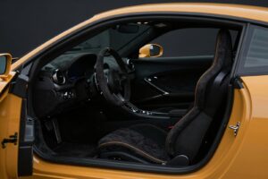 Black microfibre sports seats and steering wheel with amber stitching, seen through the open door of the coupé