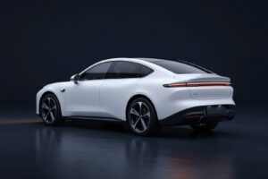 Glacier white electric saloon seen from behind, with a long roofline and slim tail lights, in a dark showroom