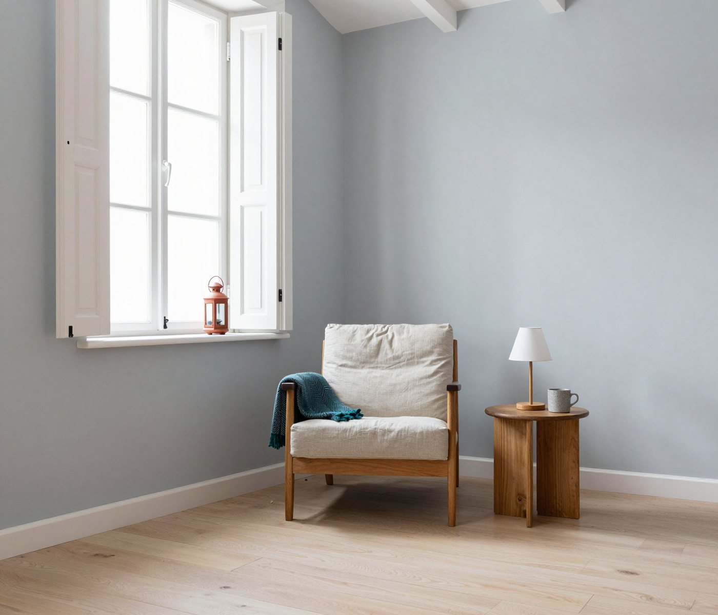 A quiet reading corner by a tall window: an oak armchair with a teal throw, and a small lamp and a mug on an oak side table