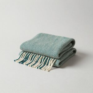 Cream and teal herringbone wool throw folded with its twisted fringe over the front edge