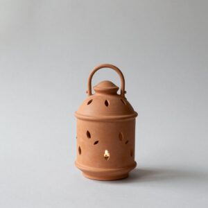 Unglazed terracotta lantern pierced with small leaf shapes, with a candle glowing inside