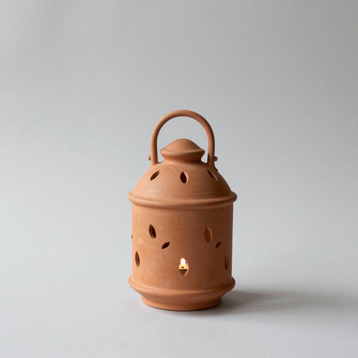 Unglazed terracotta lantern pierced with small leaf shapes, with a candle glowing inside