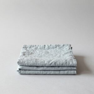 Pale blue-grey washed linen tablecloth folded into a soft, neat stack