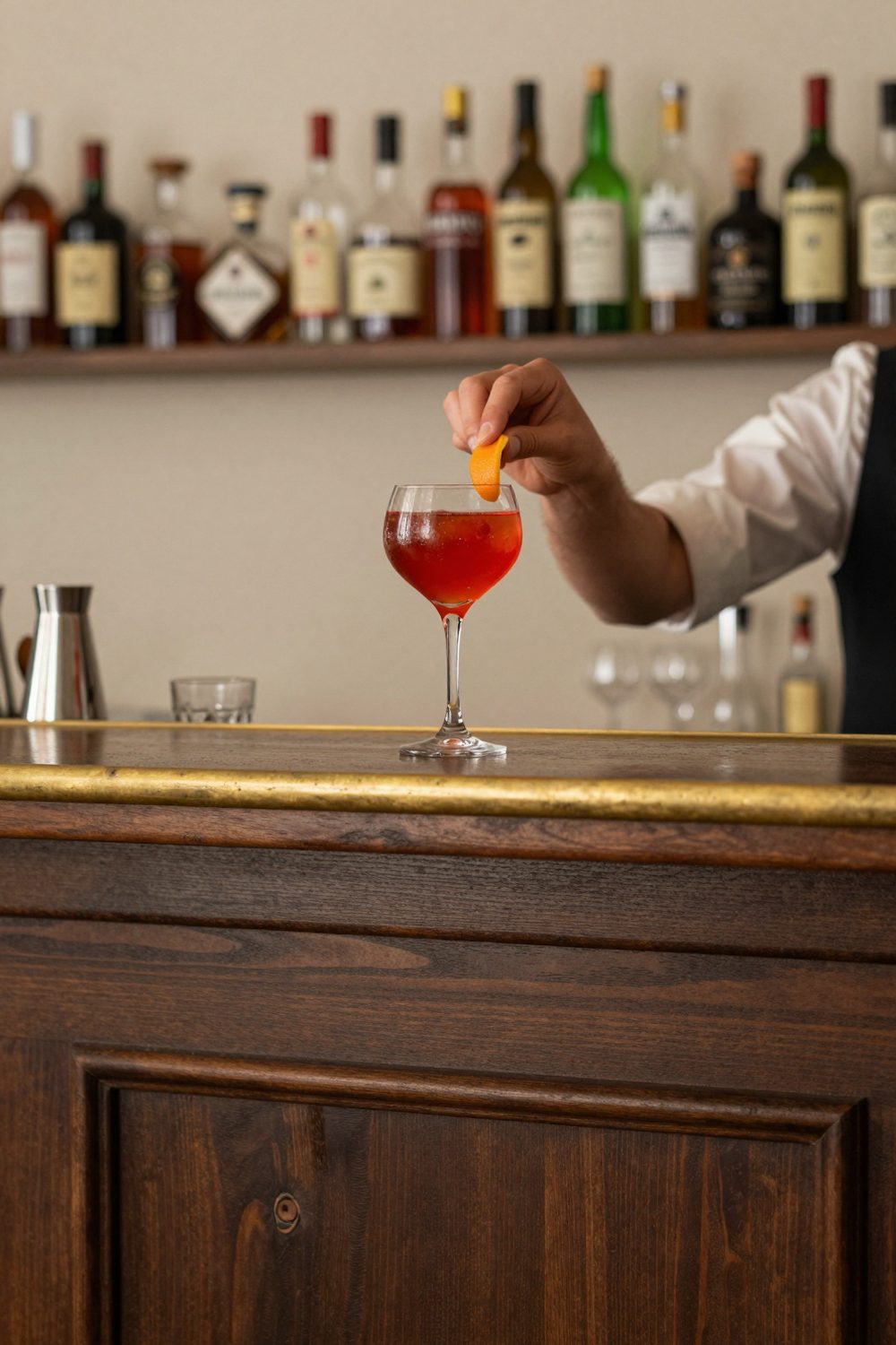 The bar counter in dark wood and brass, a cocktail being finished